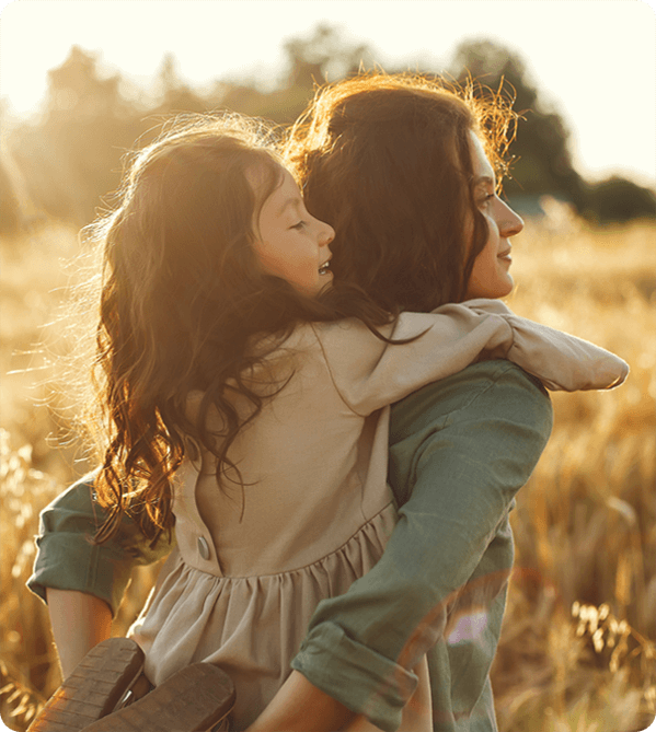 Mother carrying her young daughter in a sunlit field.